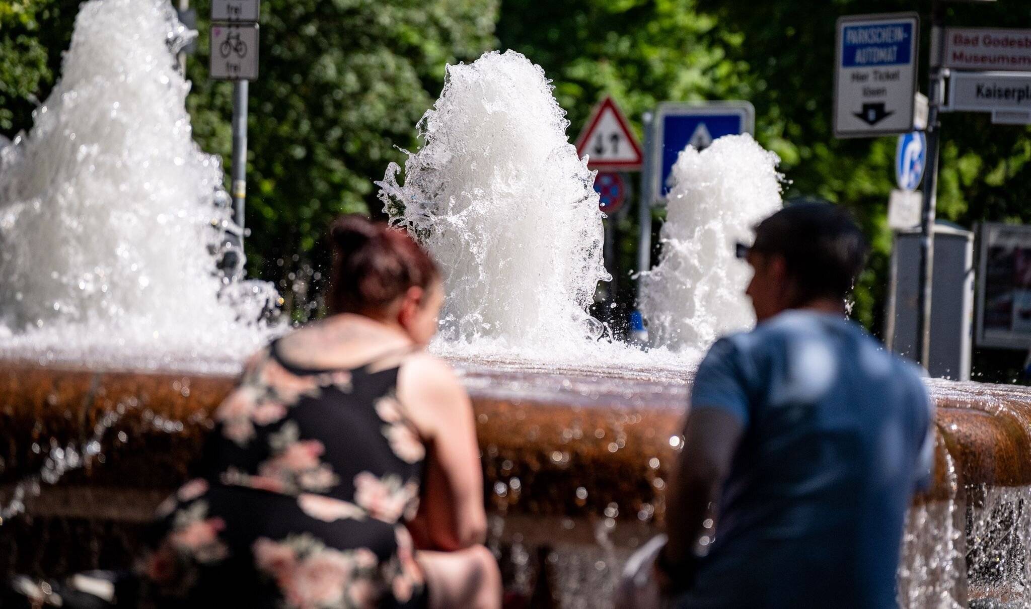 Personen in Sommerkleidung sitzen in Bonn an einem Brunnen in der Sonne