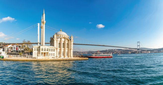  Ortak&ouml;y-Moschee am europ&auml;ischen Ufer des Bosporus mit einem Ausflugsboot und der Bosporus-Br&uuml;cke im Hintergrund.
